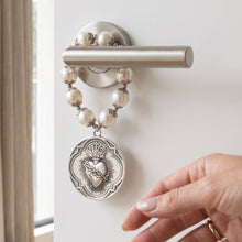 Cargar imagen en el visor de la galería, Bendición para puerta Llena de Gracia con perlas y dije de Sagrado Corazón en rodio colgada en una manija de puerta

