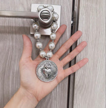 Cargar imagen en el visor de la galería, Bendición para puerta Llena de Gracia con perlas blancas y dije de Sagrado Corazón en rodio colgada en una manija.

