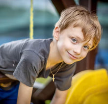 Cargar imagen en el visor de la galería, Niño sonriente usando collar Mi Primera Cruz de Llena de Gracia en plata 925 chapada en oro 18k en un parque
