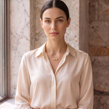Cargar imagen en el visor de la galería, Mujer luciendo collar Llena de Gracia con dije de tres corazones en oro vermeil de 18k sobre camisa color crema
